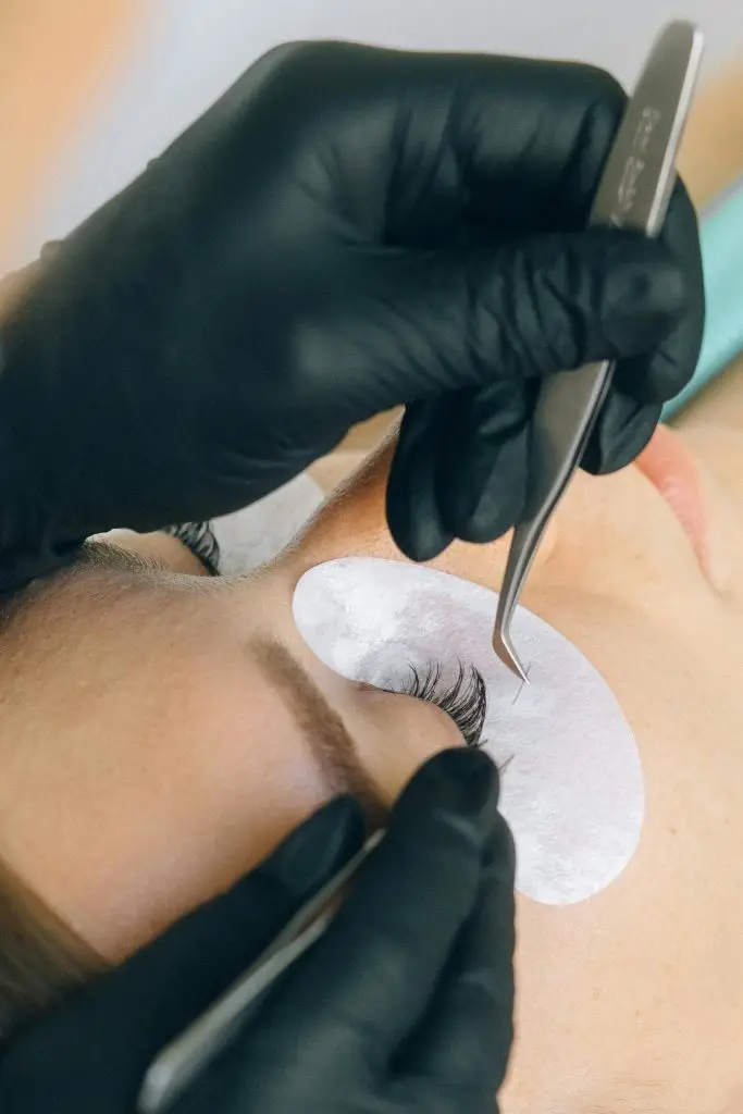 Close-up of eyelash extension application with black gloves and tweezers.